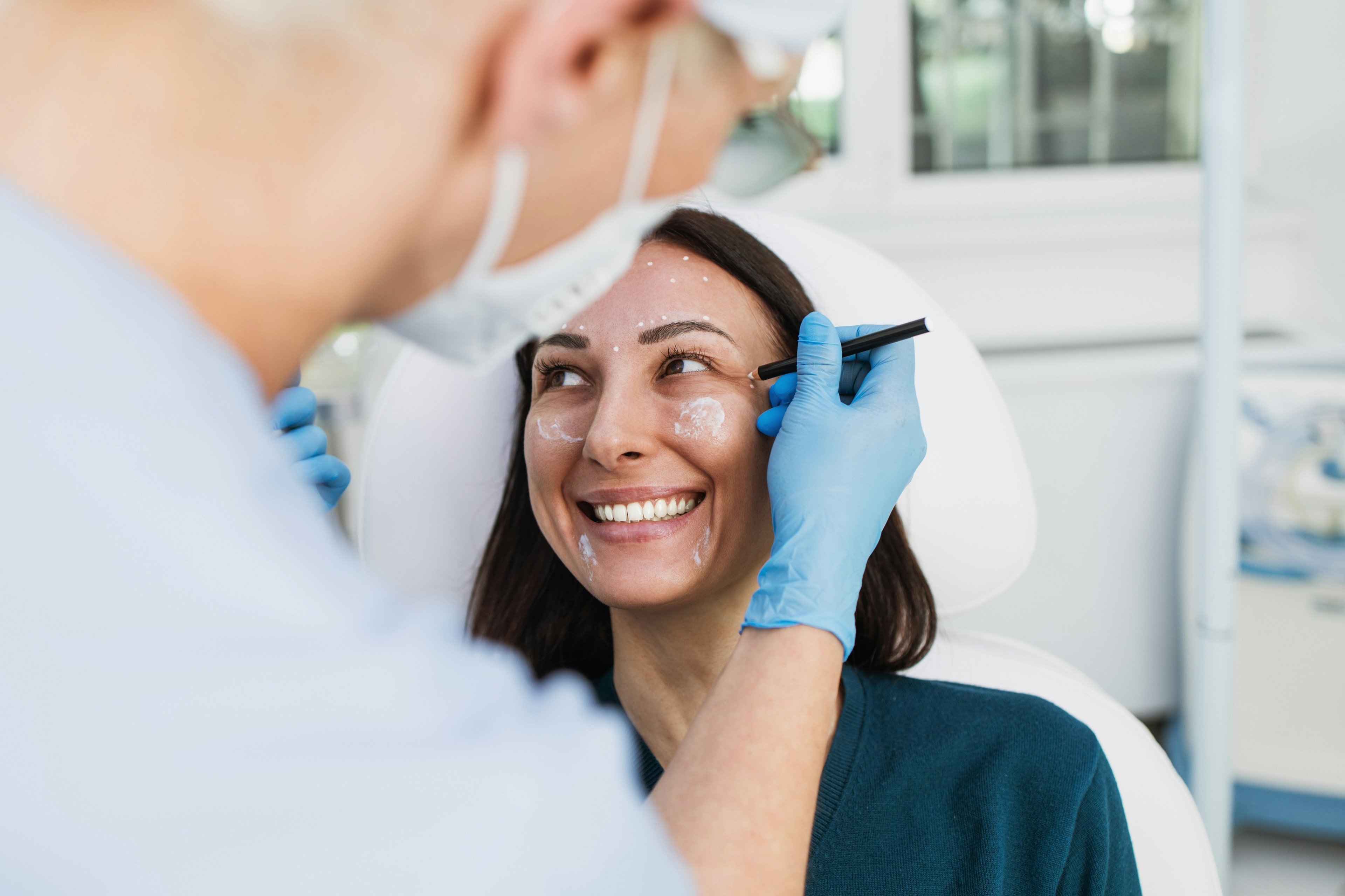 A practitioner marking treatment points on a smiling patient's face during a consultation